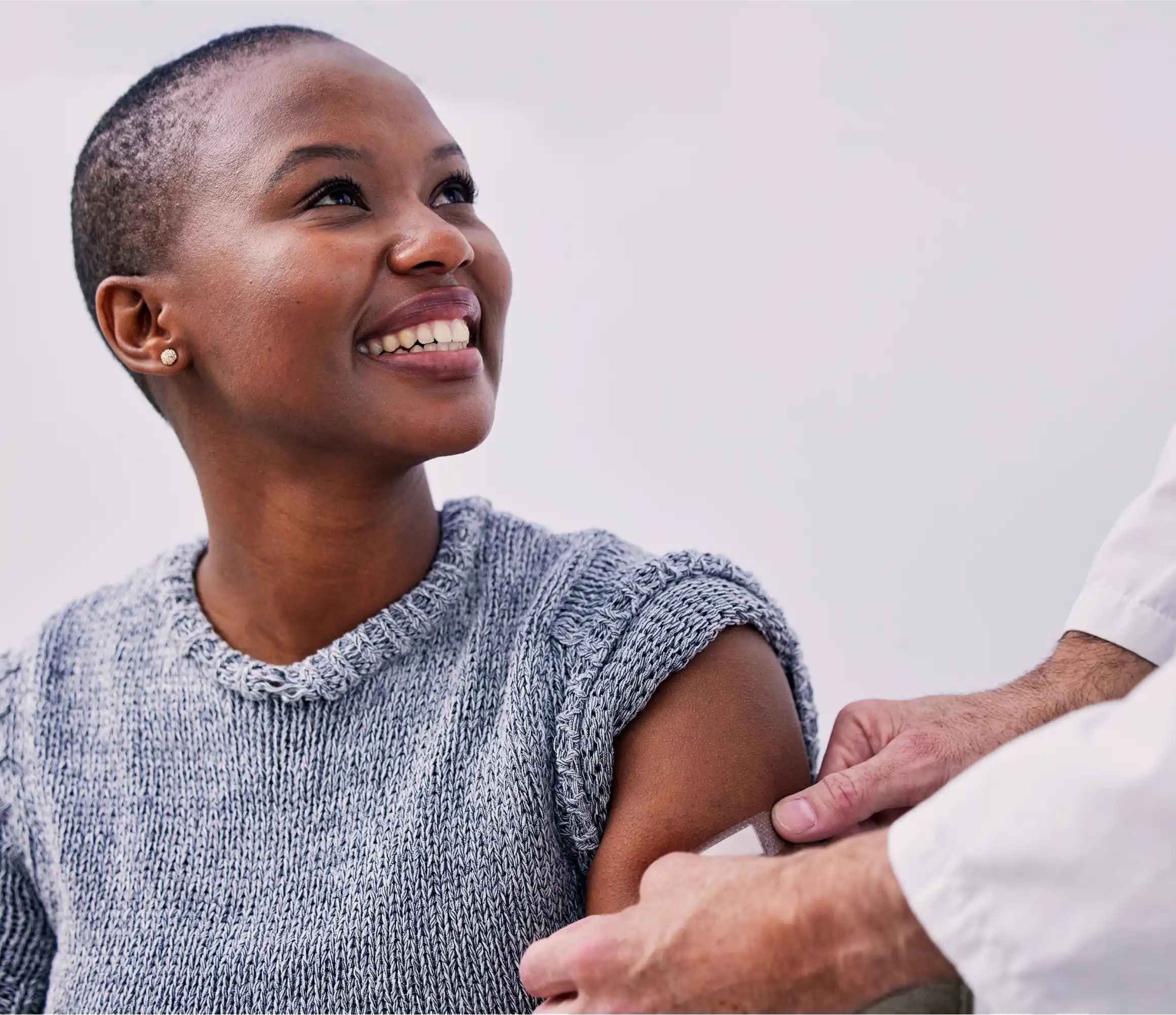Smiling African American patient with short hair in gray sweater, receiving primary care from a healthcare professional